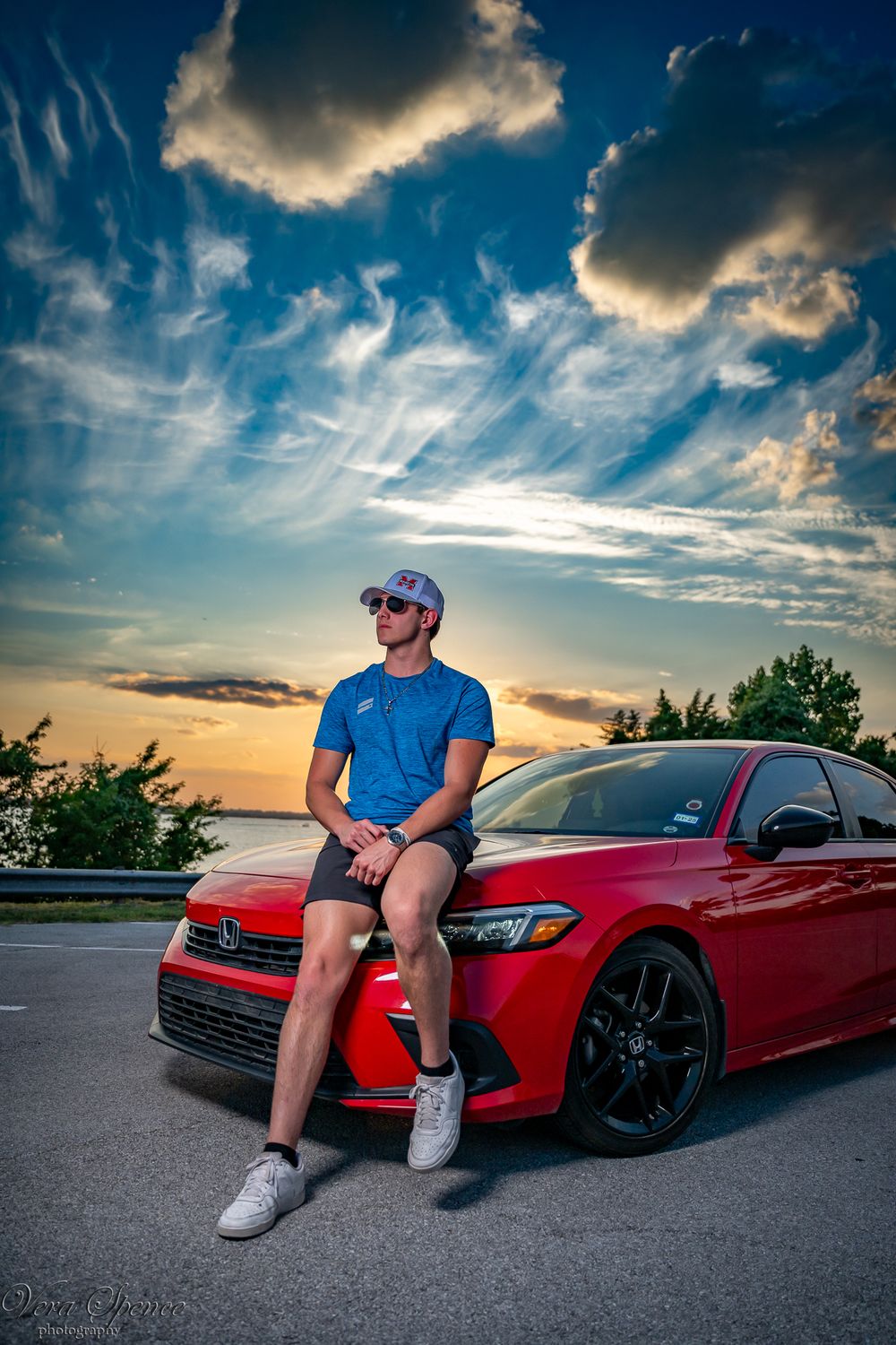 Senior with his red Volkswagen car parked during a dramatic sunset with clouds in the background.