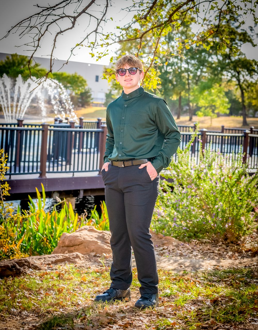 A teenager in dark green button-down shirt poses casually by garden railing.