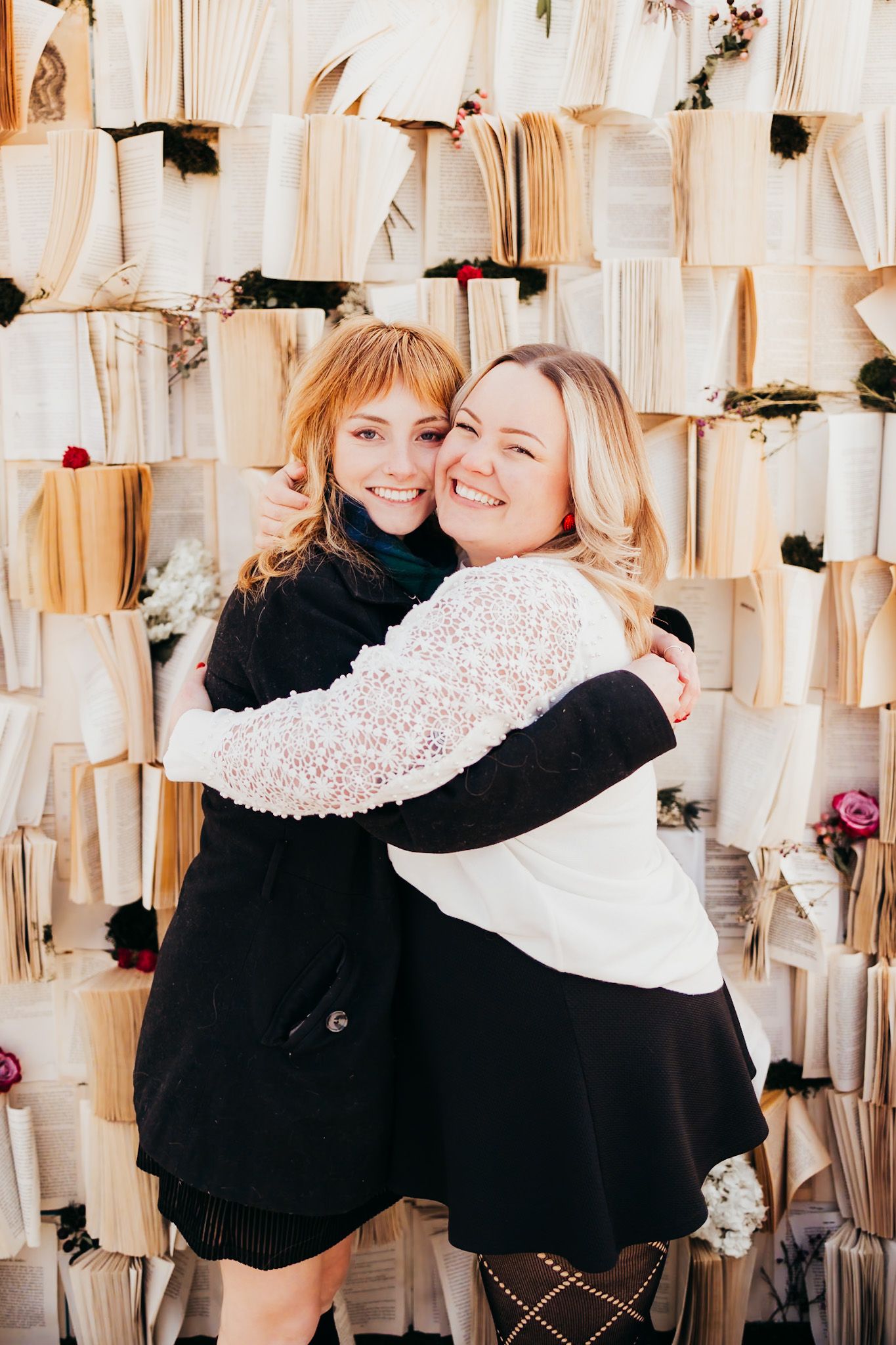 two girl best friends hugging in front of a wall made of books