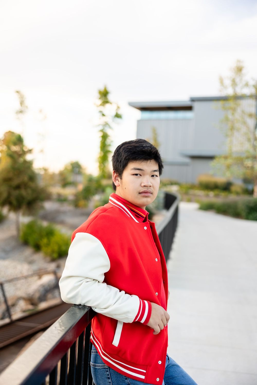 A person in a red varsity jacket poses outdoors against a blurred urban background.