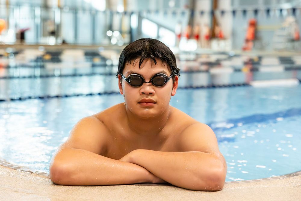 Swimmer resting at edge of indoor pool with lane lines visible in background.