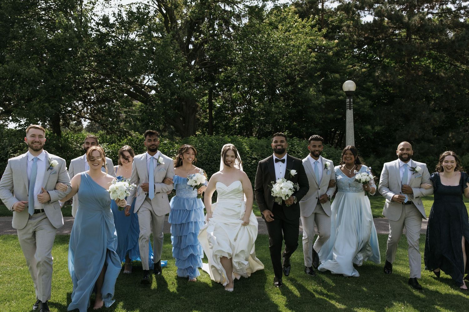 Wedding party in coral dresses gathers outdoors with church building in background.