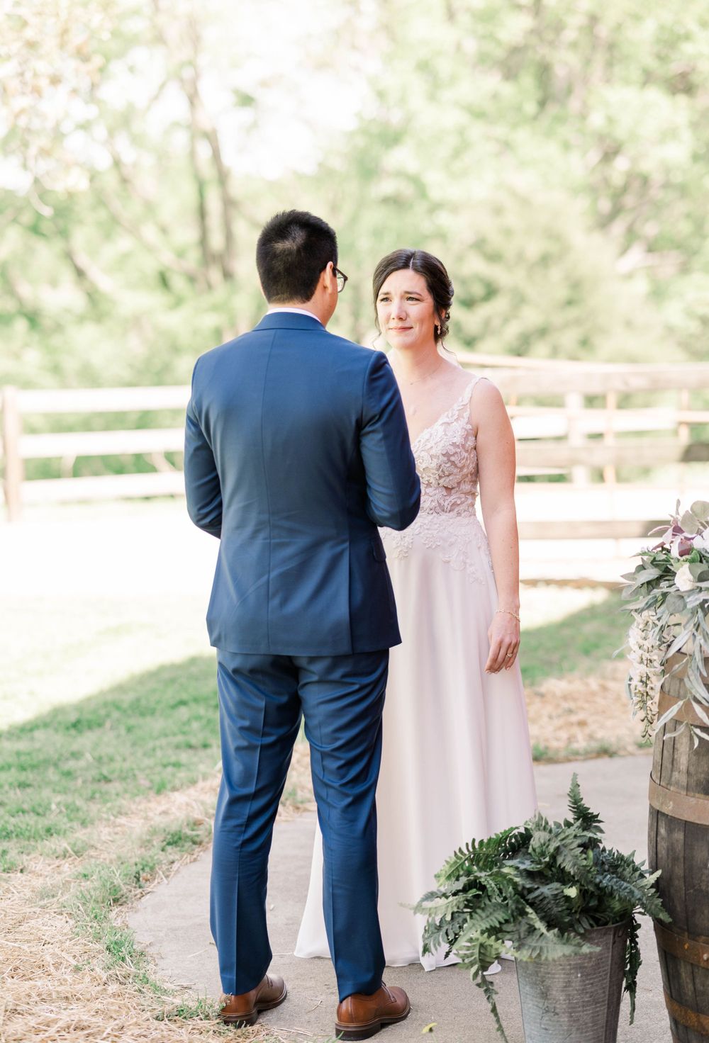 A couple in wedding attire stands together on a rustic path with natural greenery in the background.