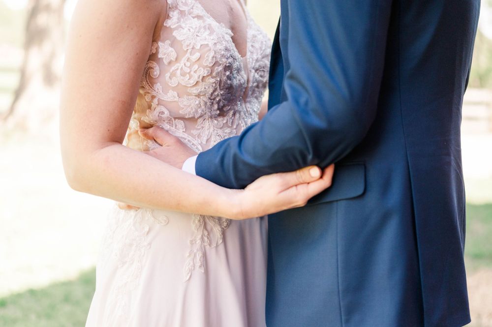 Close-up detail of wedding attire showing a delicate lace dress and navy suit.