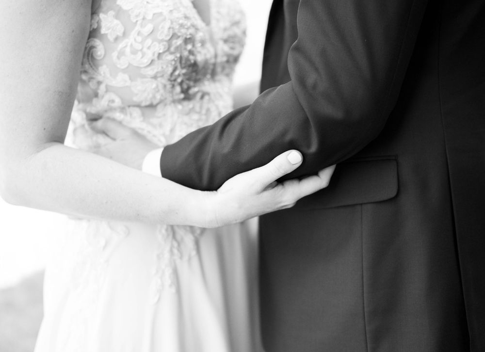A black and white detail shot of gentle hands touching during an intimate wedding moment.