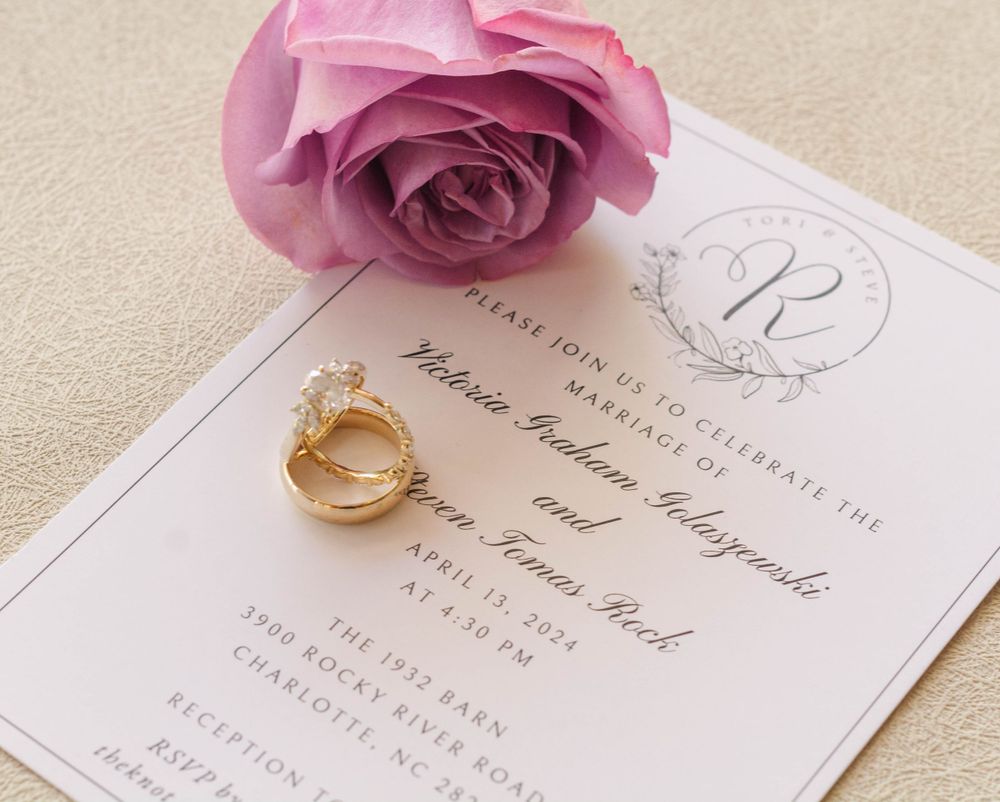 Wedding invitation with pink rose and gold rings on beige background.