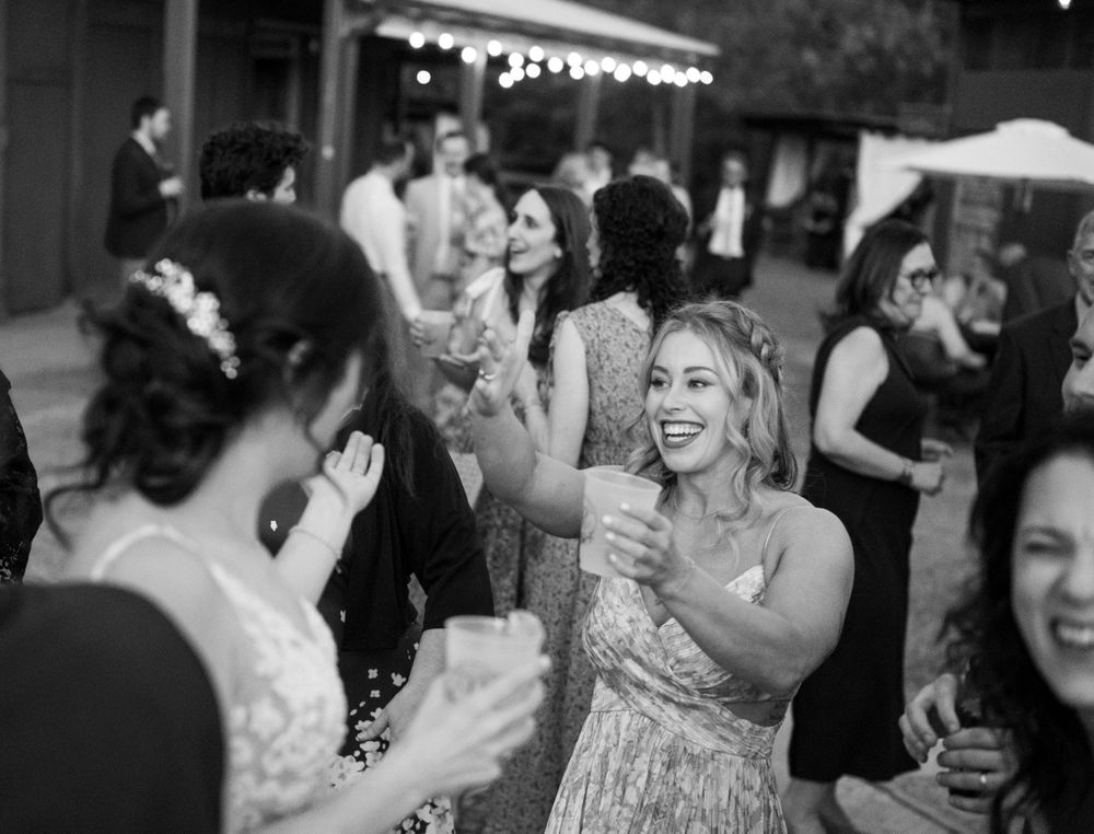 Party guests celebrate and dance at an outdoor evening reception with string lights.