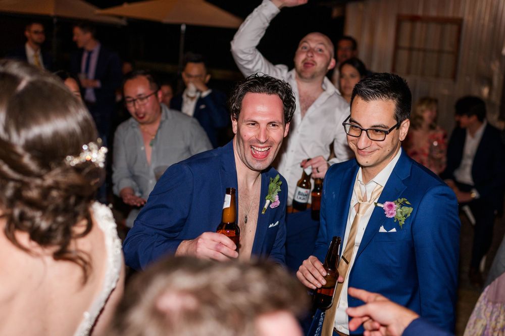 Wedding celebration with guests dancing and celebrating in formal attire under indoor lighting.