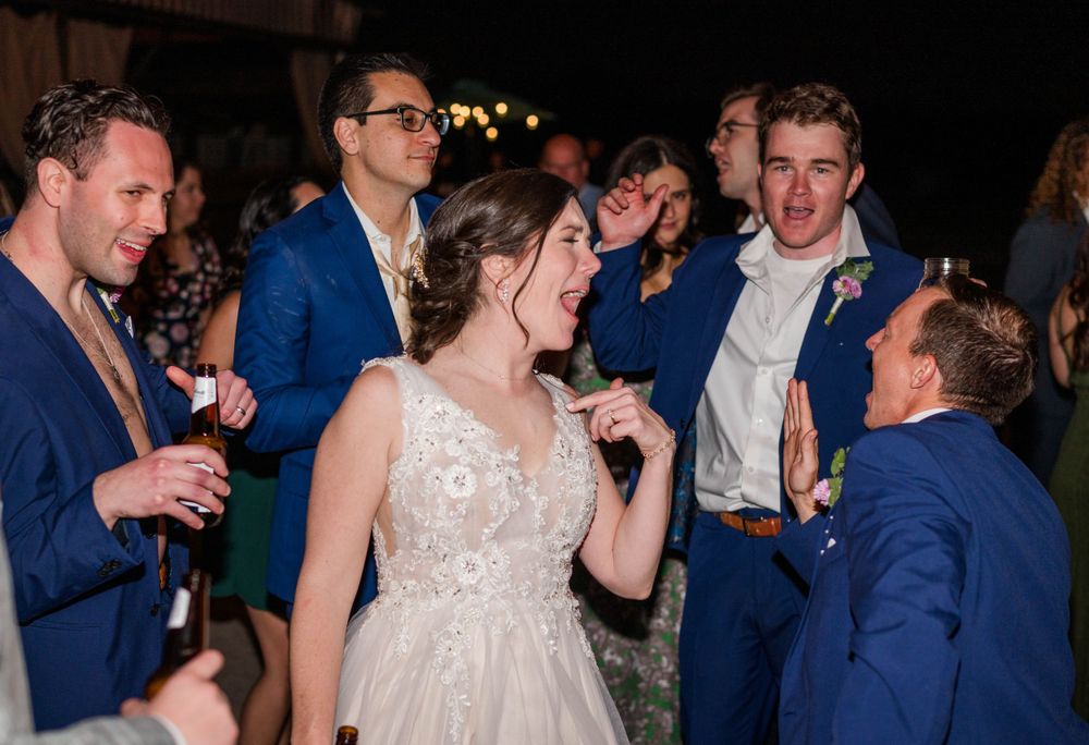 Wedding celebration with guests in navy suits dancing at an evening reception.