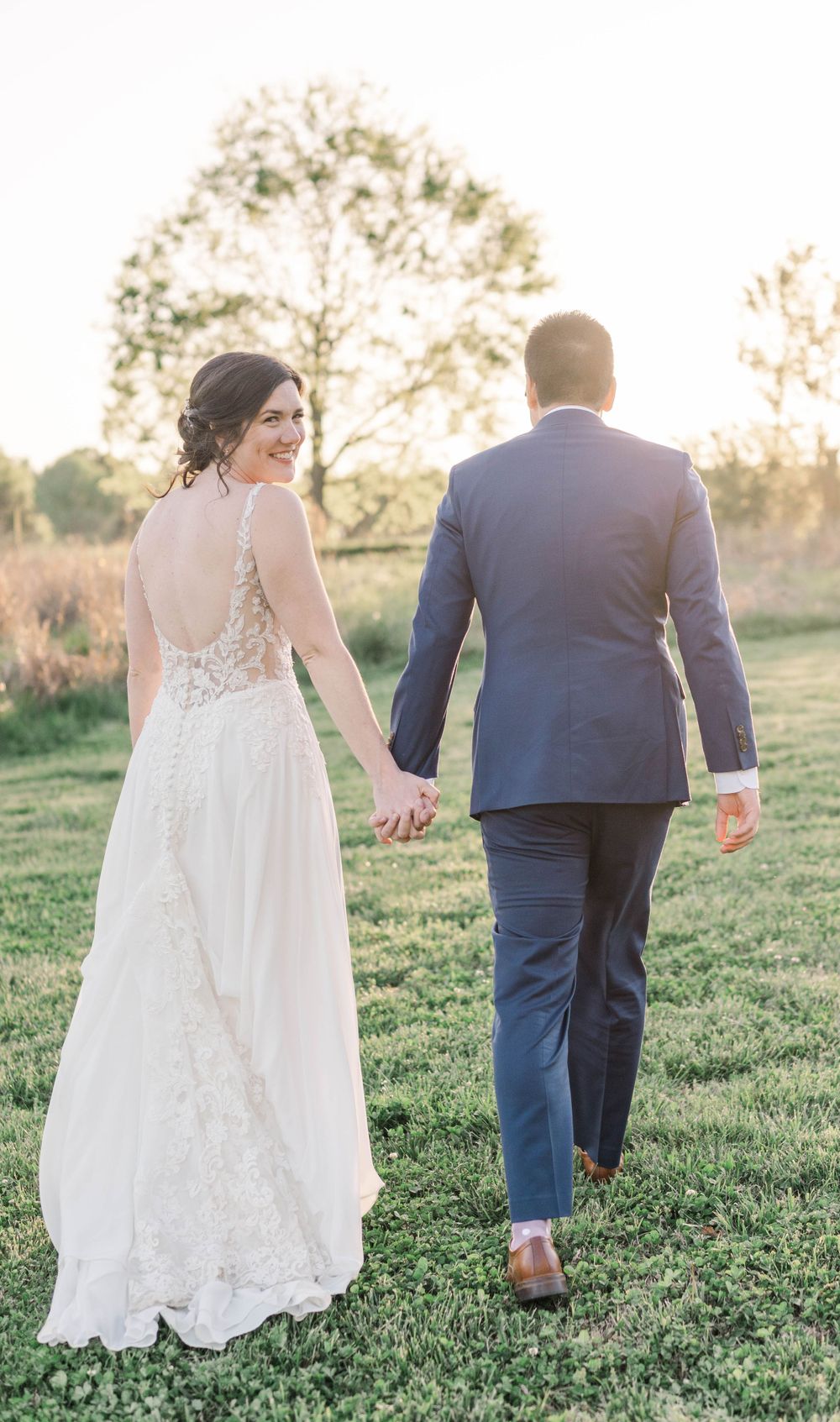 Couple walking hand in hand across grassy field in wedding attire. The 1932 Barn Venue, Charlotte, NC