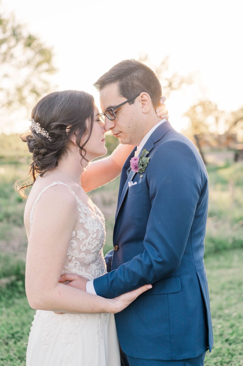 Intimate wedding portrait of couple in navy suit and lace dress against warm evening light.