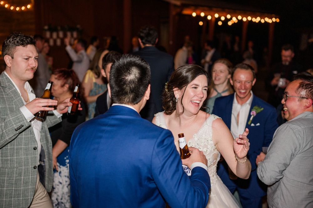 Wedding reception guests dancing and laughing together under string lights at an evening celebration.