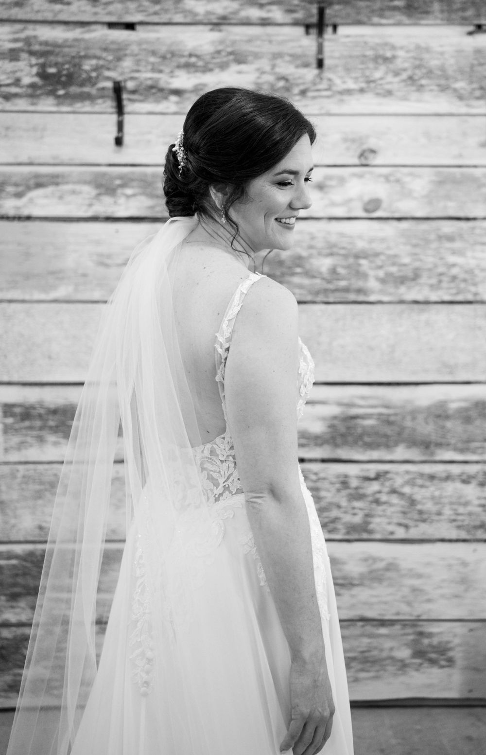 Elegant black and white photo of bride in flowing veil against weathered wood background.