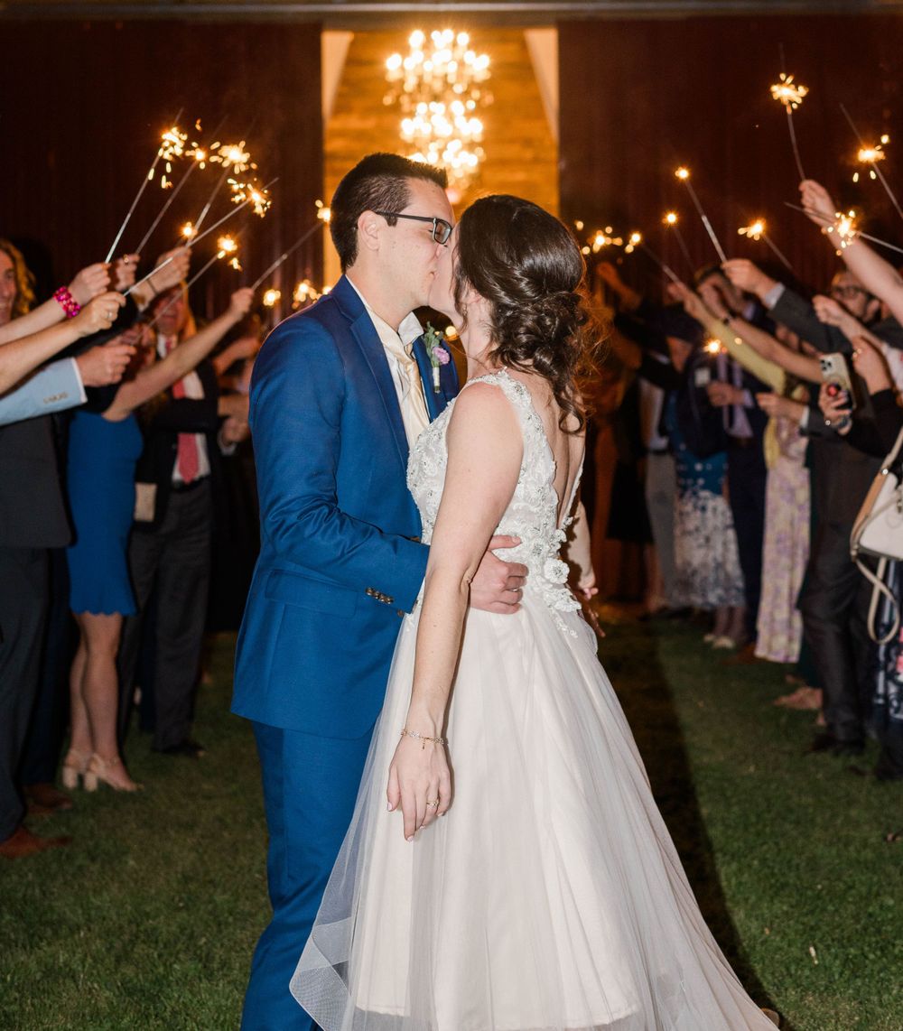 Wedding couple shares a romantic moment under sparklers held by guests at nighttime ceremony. The 1932 Barn Venue, Charlotte, NC