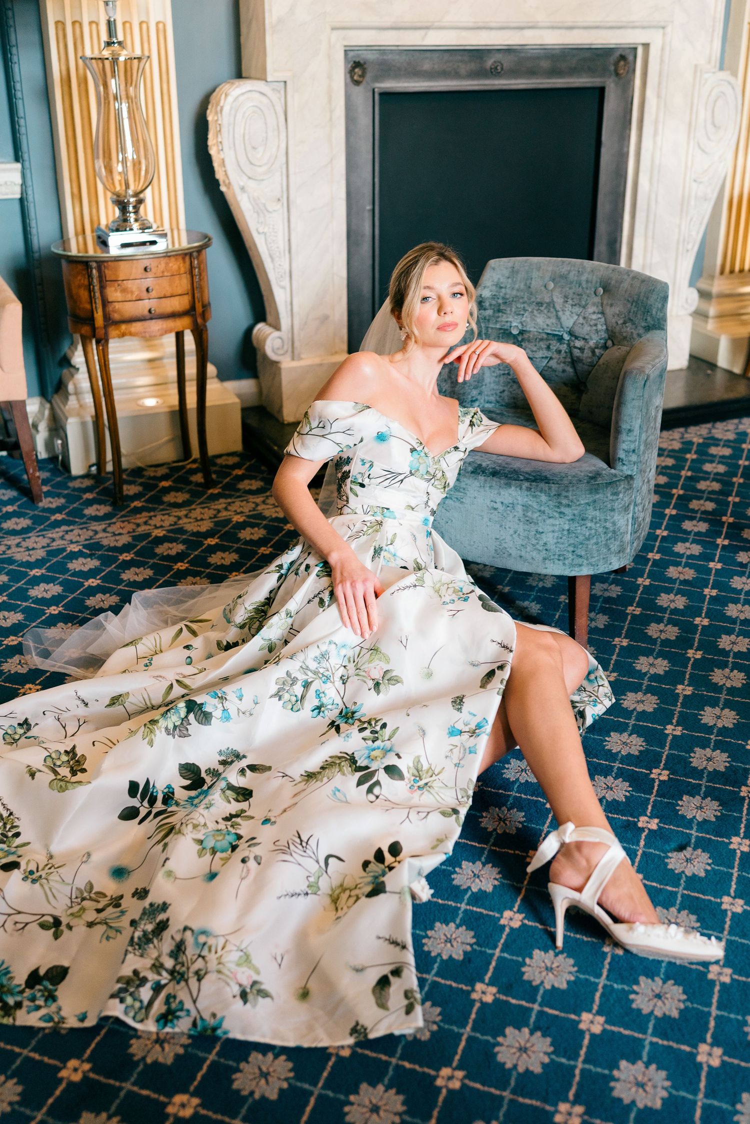 Elegant floral dress photoshoot on blue patterned carpet near a fireplace.