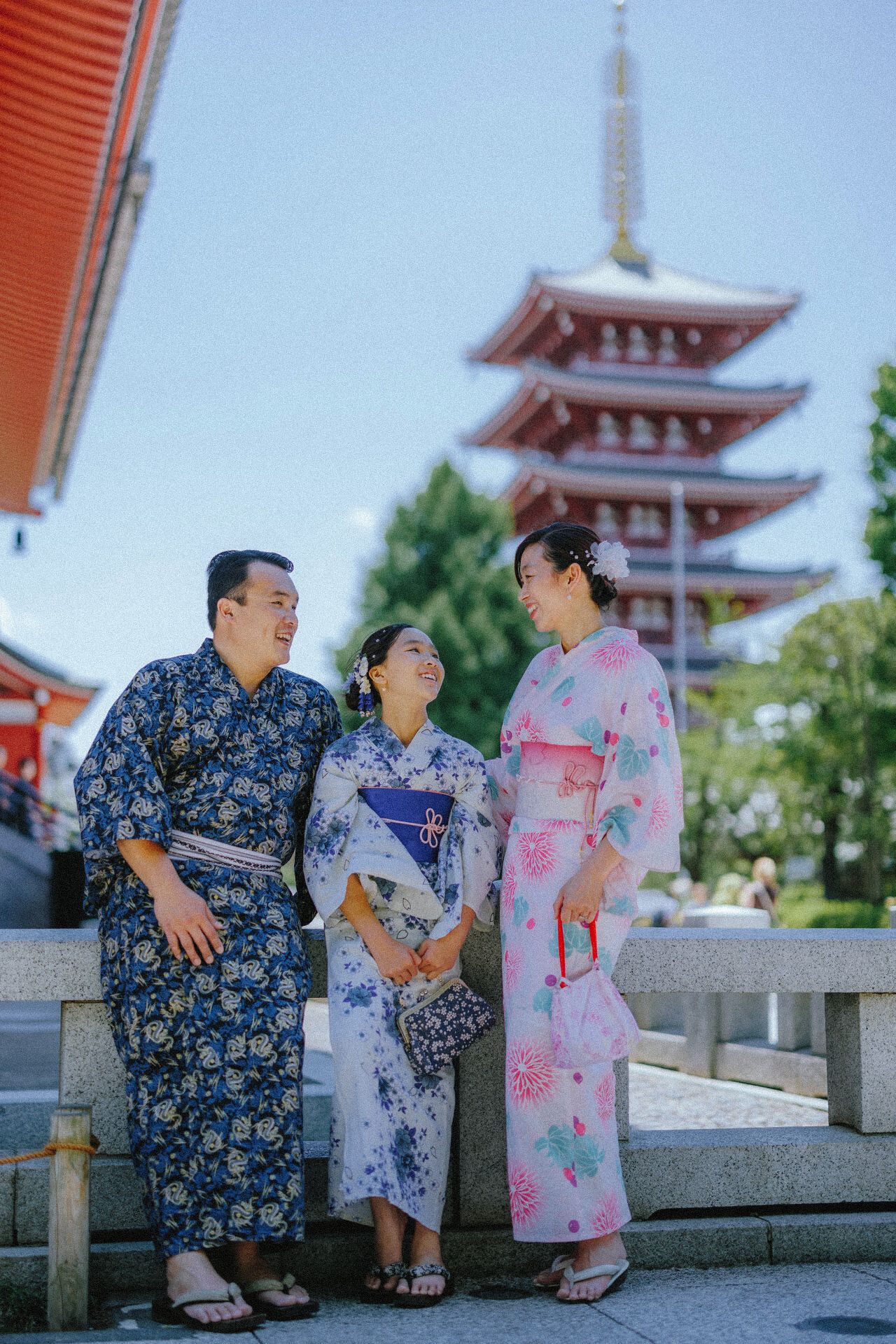Three people in traditional yukata posing in front of five-story pagoda at Japanese temple.