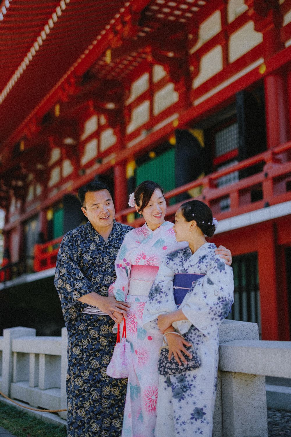 Group wearing yukata kimono having conversation outside traditional red temple building in Japan.