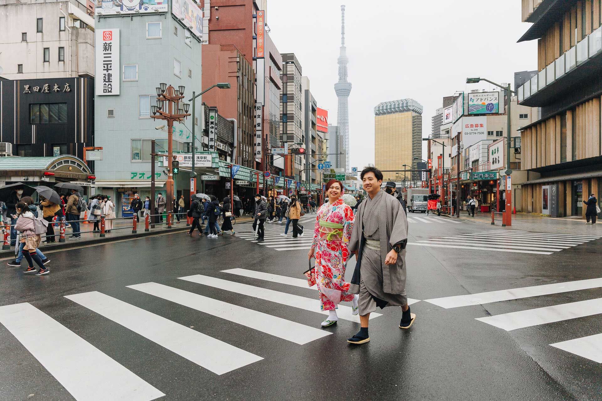 Couple in traditional Japanese clothing crossing a street with Tokyo Skytree visible.