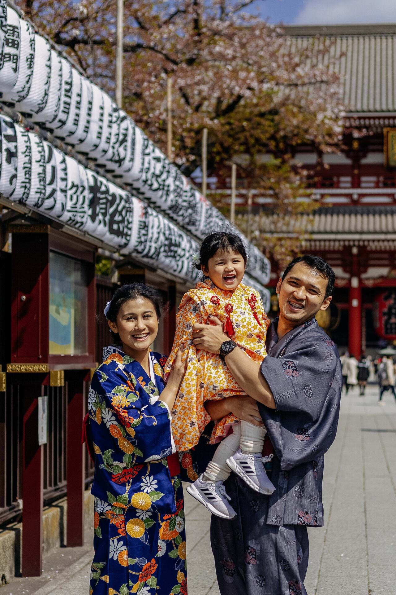 A family wearing traditional Japanese yukata poses together at a temple with white paper lanterns in the background.