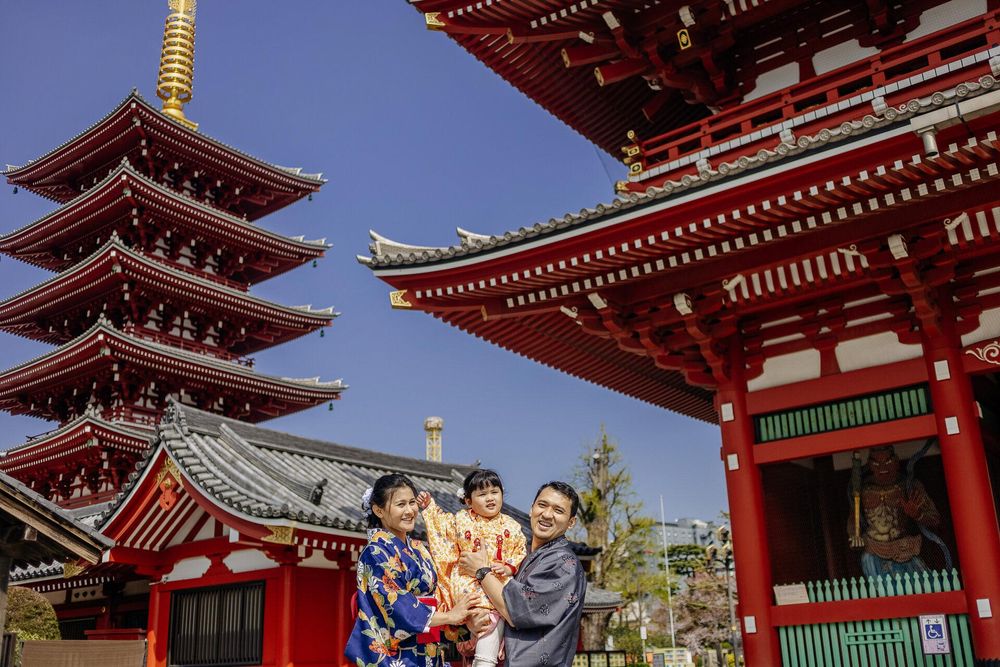 Red pagodas of Sensoji Temple frame visitors in traditional Japanese dress against blue sky.