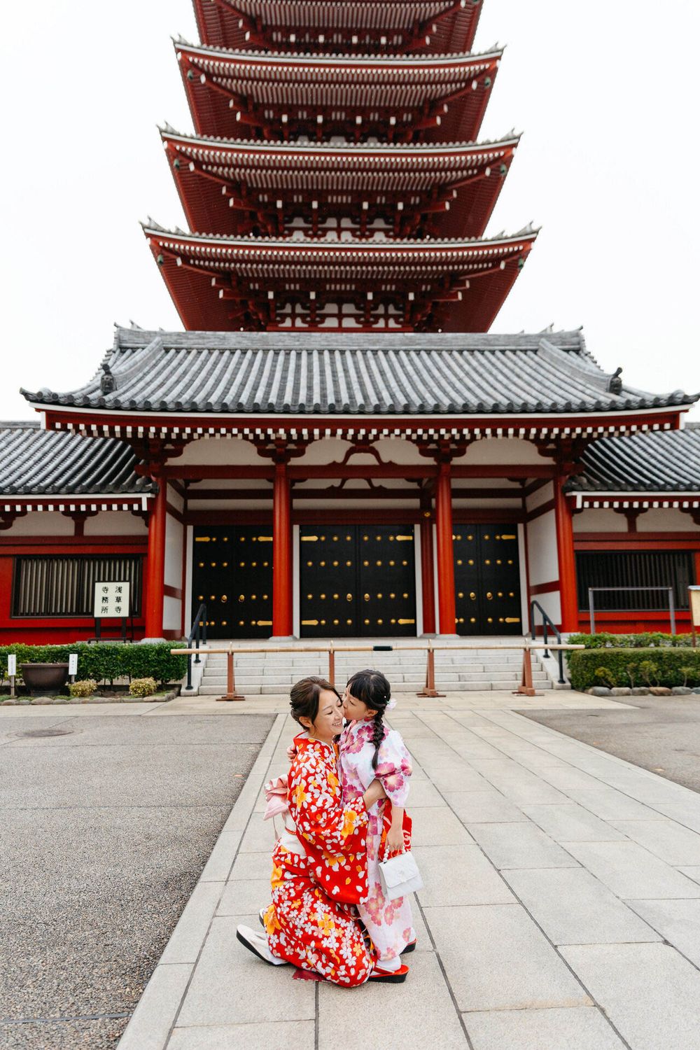 Two people in vibrant floral kimonos pose together in front of a five-tiered pagoda.