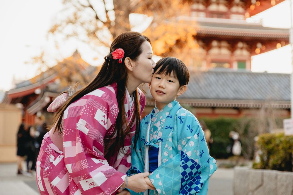 A tender moment between two people wearing pink and blue yukatas in front of a temple structure.
