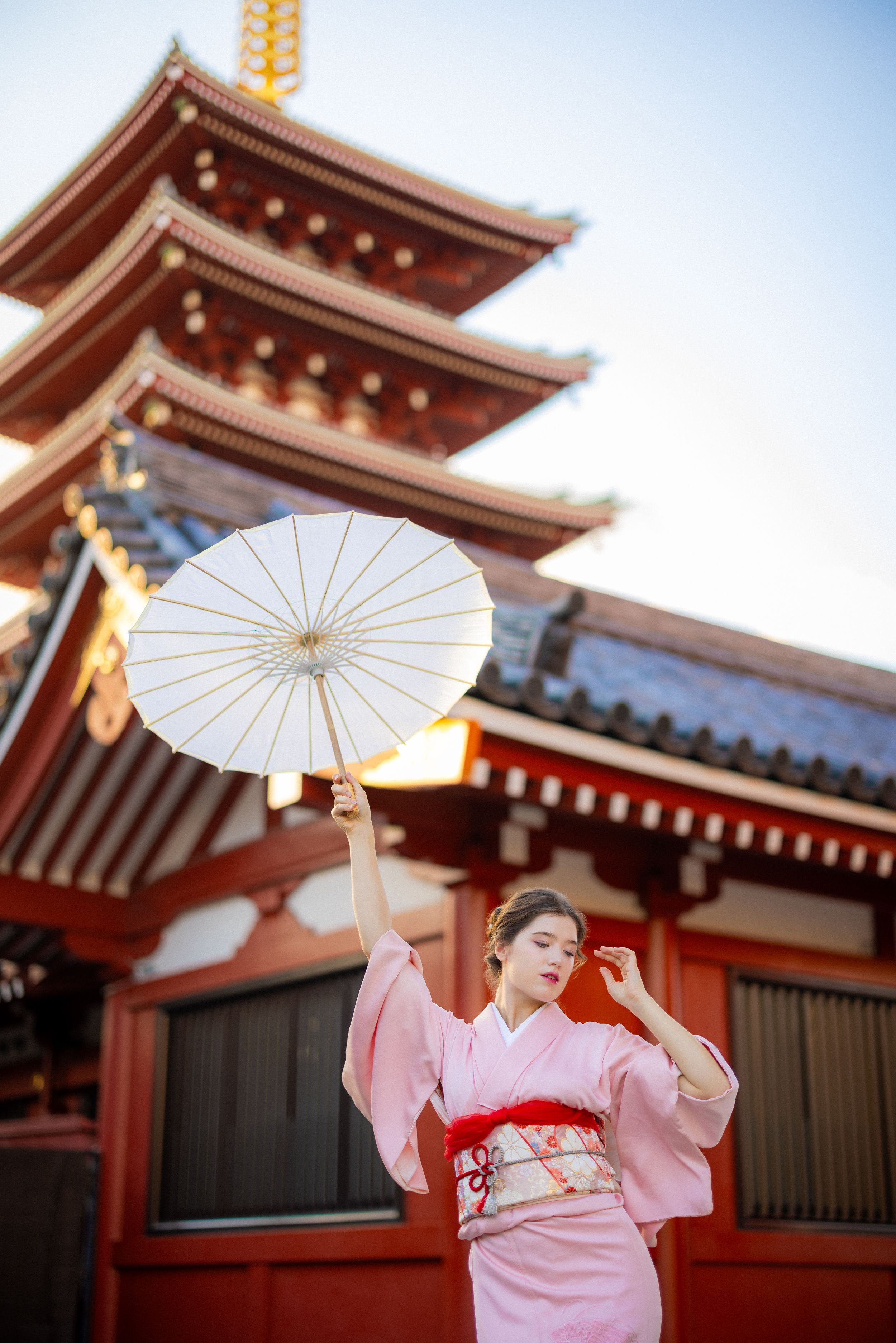Person in pink kimono holds white parasol in front of traditional Japanese pagoda.