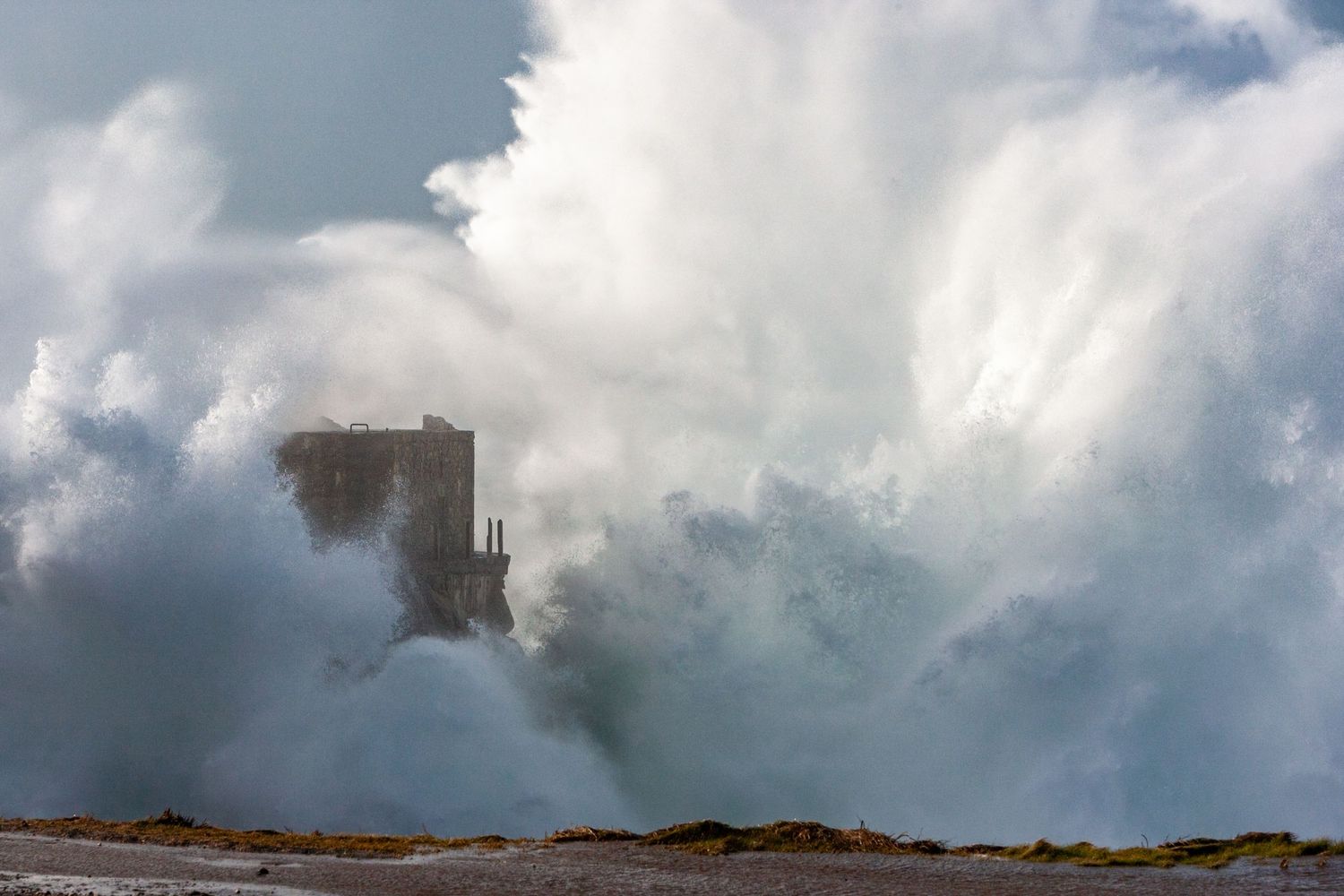 Massive wave crashing against coastal rocks creating a dramatic spray against cloudy skies.