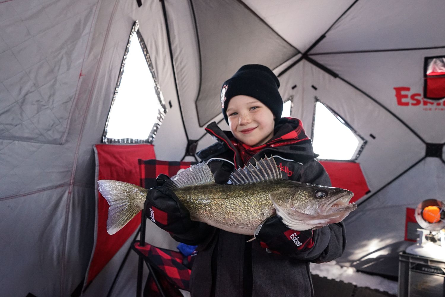 Ice fishing success shown inside red portable shelter with multiple caught fish.