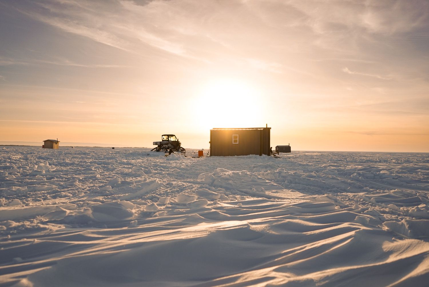Panoramic winter landscape with snowmobiles and equipment silhouetted against sunset sky.