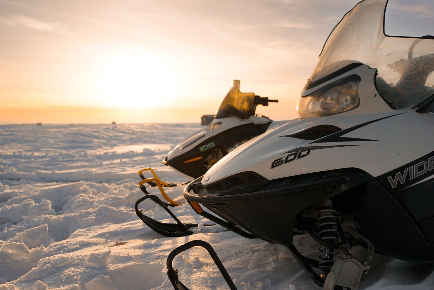 Snowmobile silhouetted against golden winter sunset on snowy terrain.