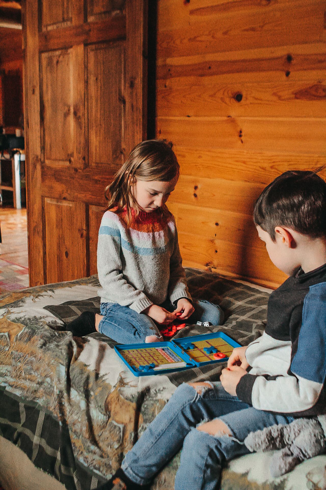 Children playing games and relaxing on a bed in a rustic cabin setting.