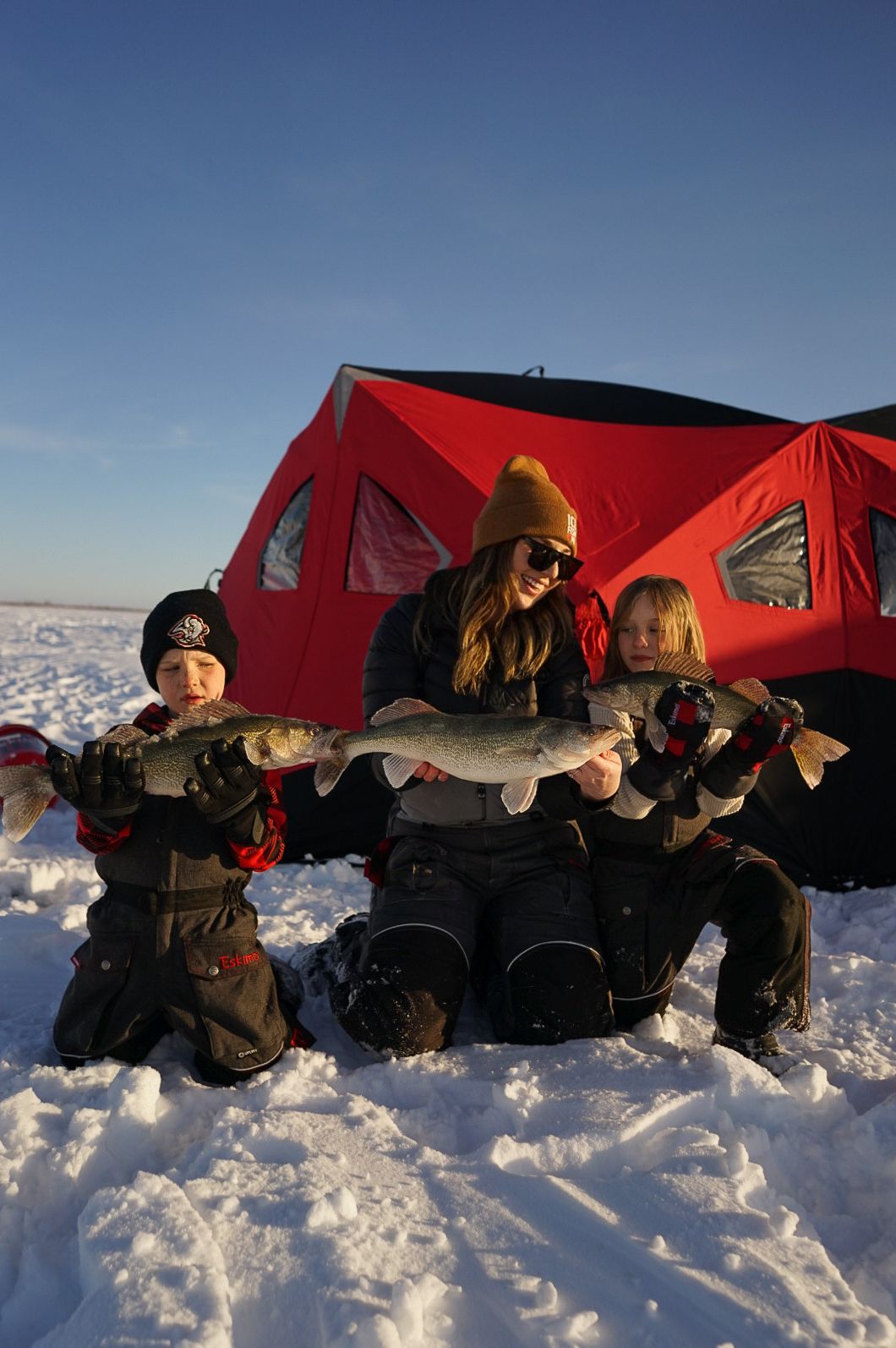 Group displaying caught fish while kneeling in snow by red ice fishing tents.
