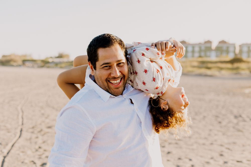 Romi laying down on her father shoulder with her face up while he is walking and playing with her.