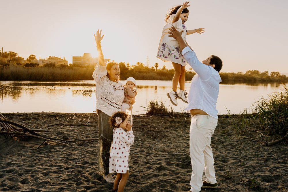 Family picture where the father lift his daughter to the sky and mom with two other children happy lifting her hand up.