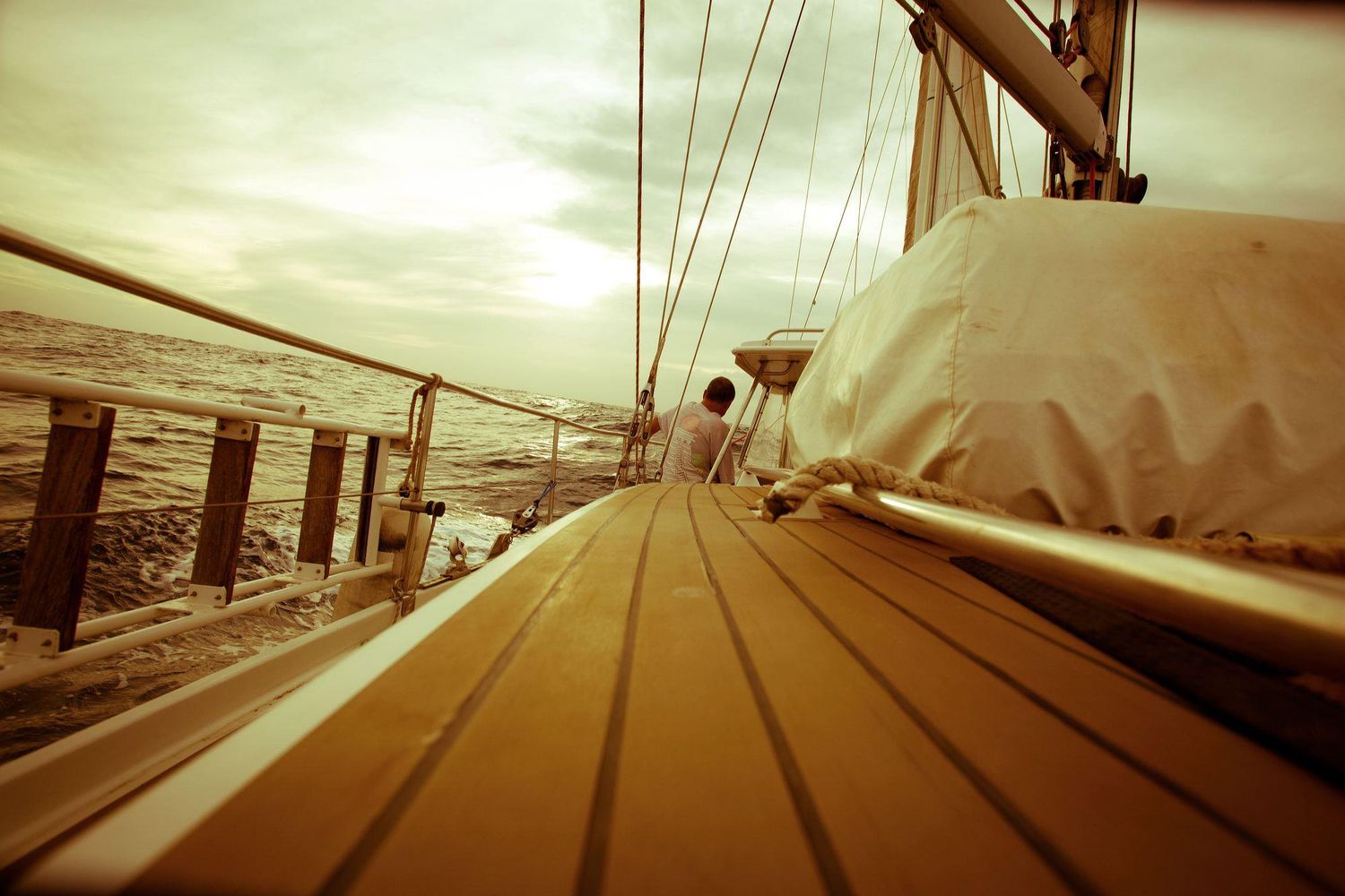 Sepia-toned view along the deck of a sailboat with canvas cover and ocean horizon.