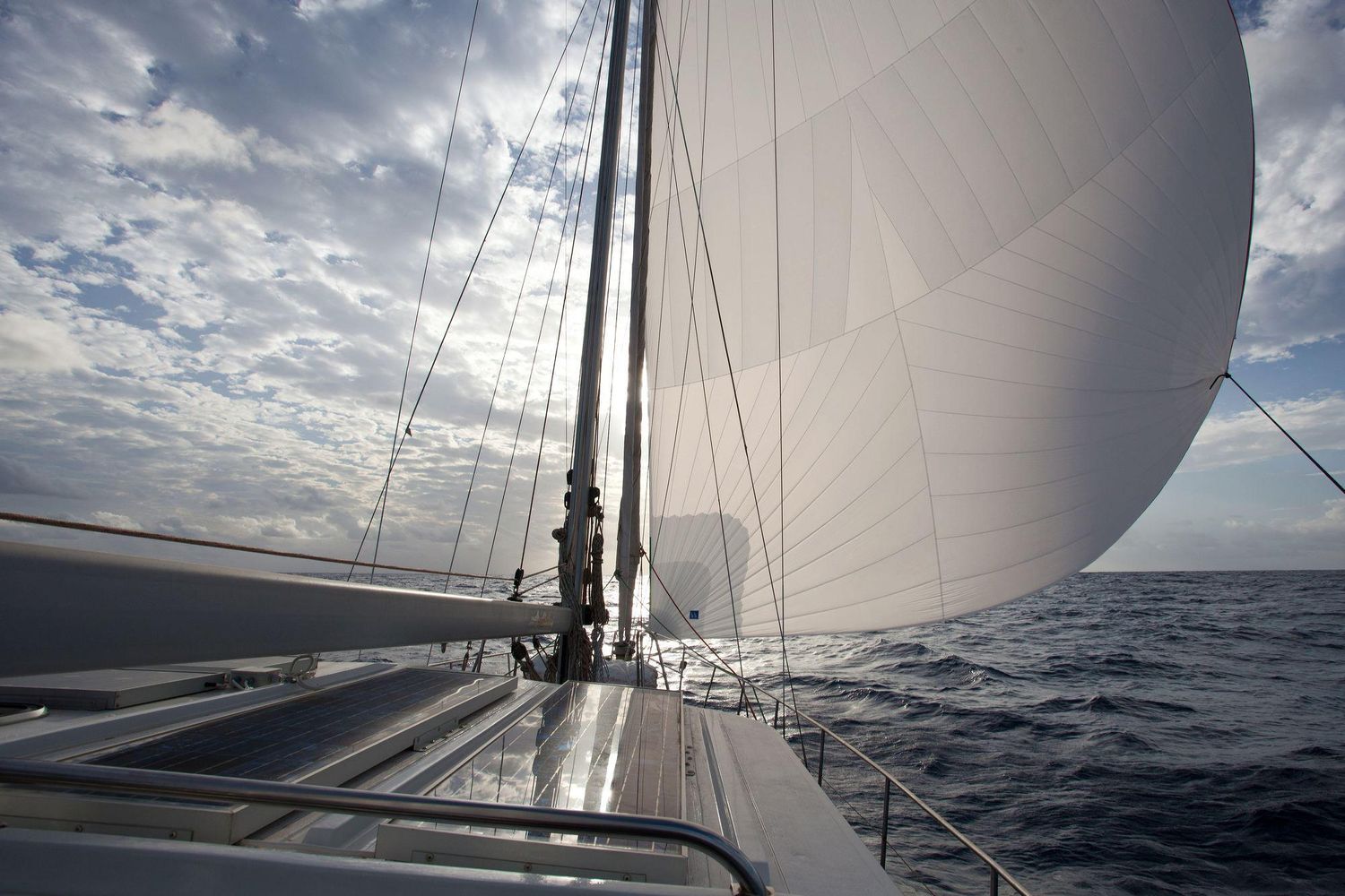 White sail billowing against dramatic cloudy sky viewed from yacht deck.
