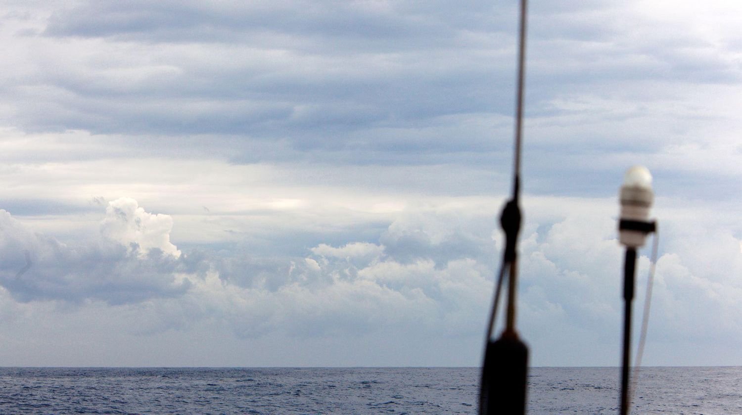 Sailing equipment and navigation instruments silhouetted against cloudy ocean horizon.