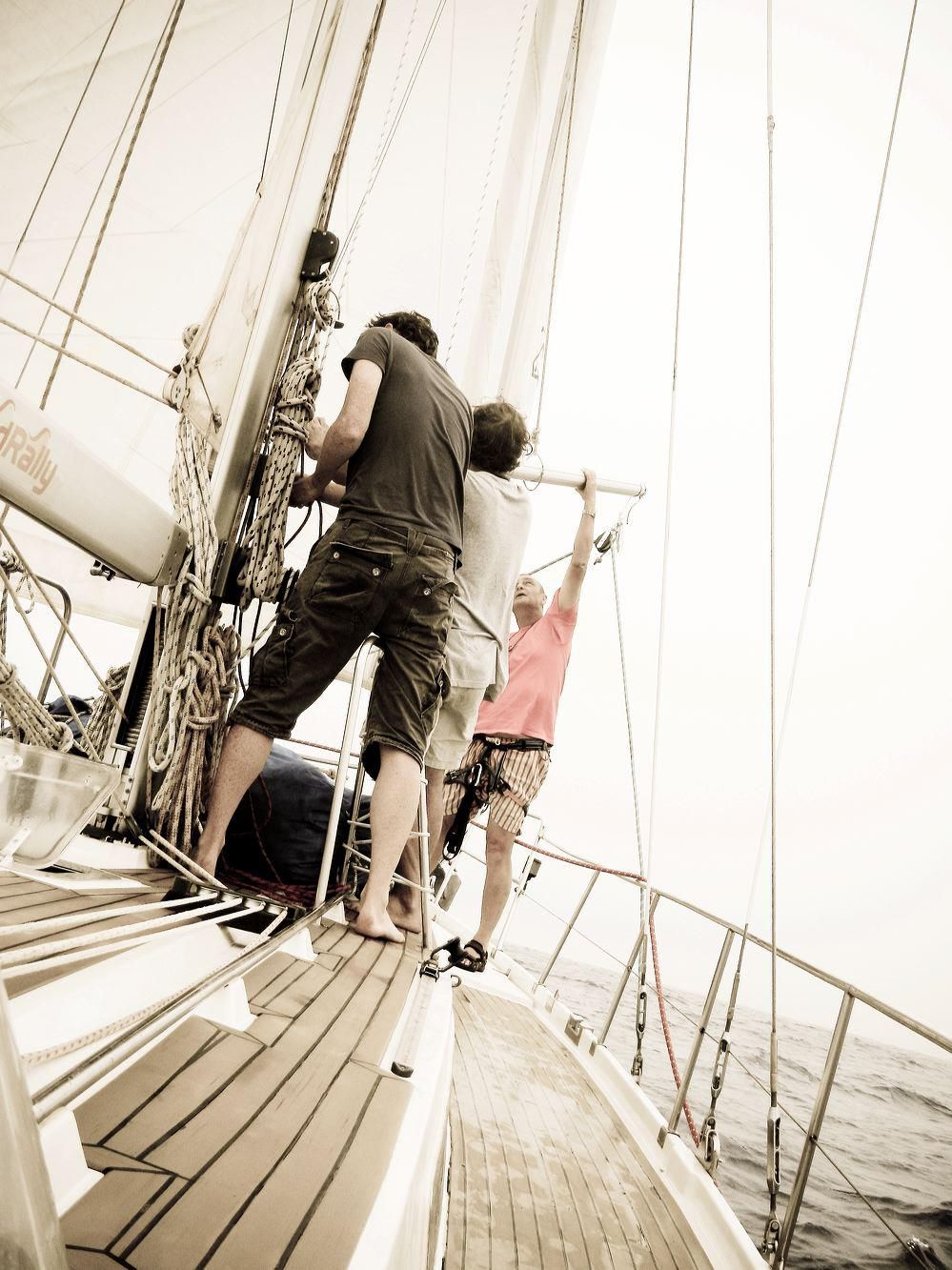Crew members working on deck of a sailboat with rigging and sails visible.