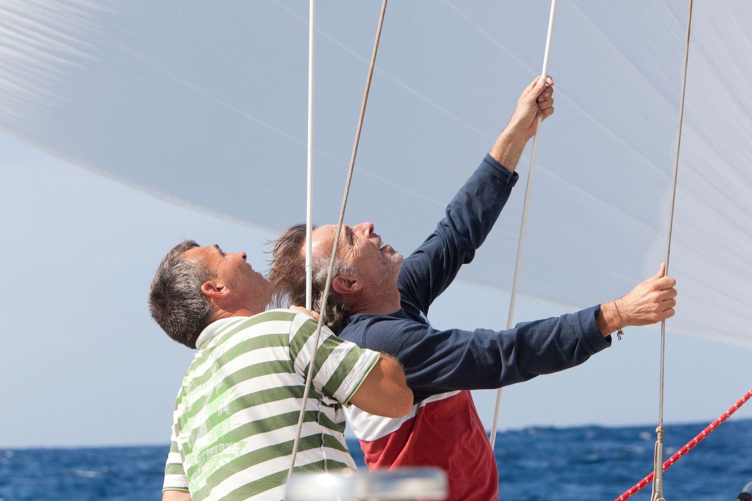 Two sailors adjusting rigging ropes on a sailing vessel at sea.