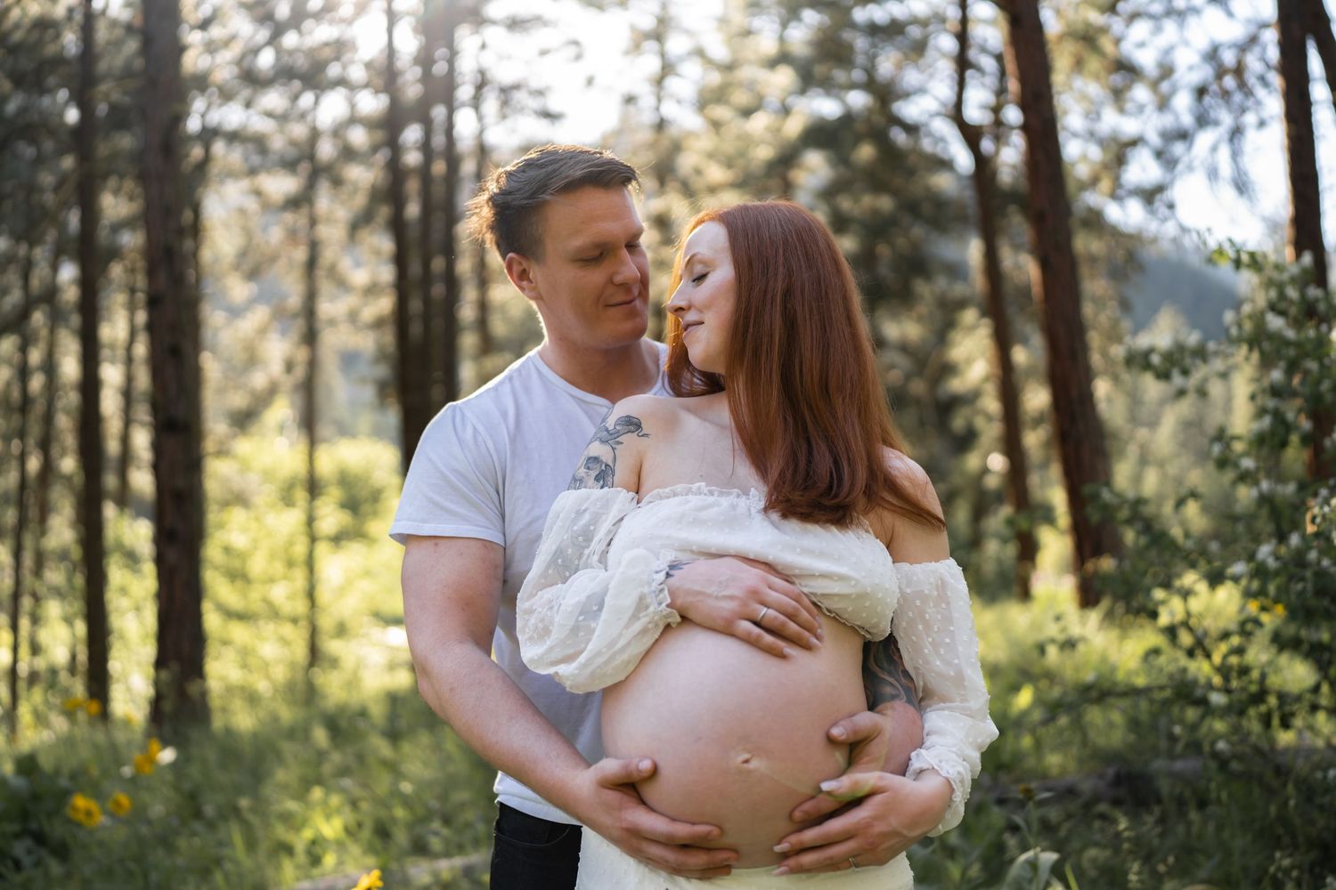 An intimate maternity portrait in a forest setting with golden sunlight filtering through.