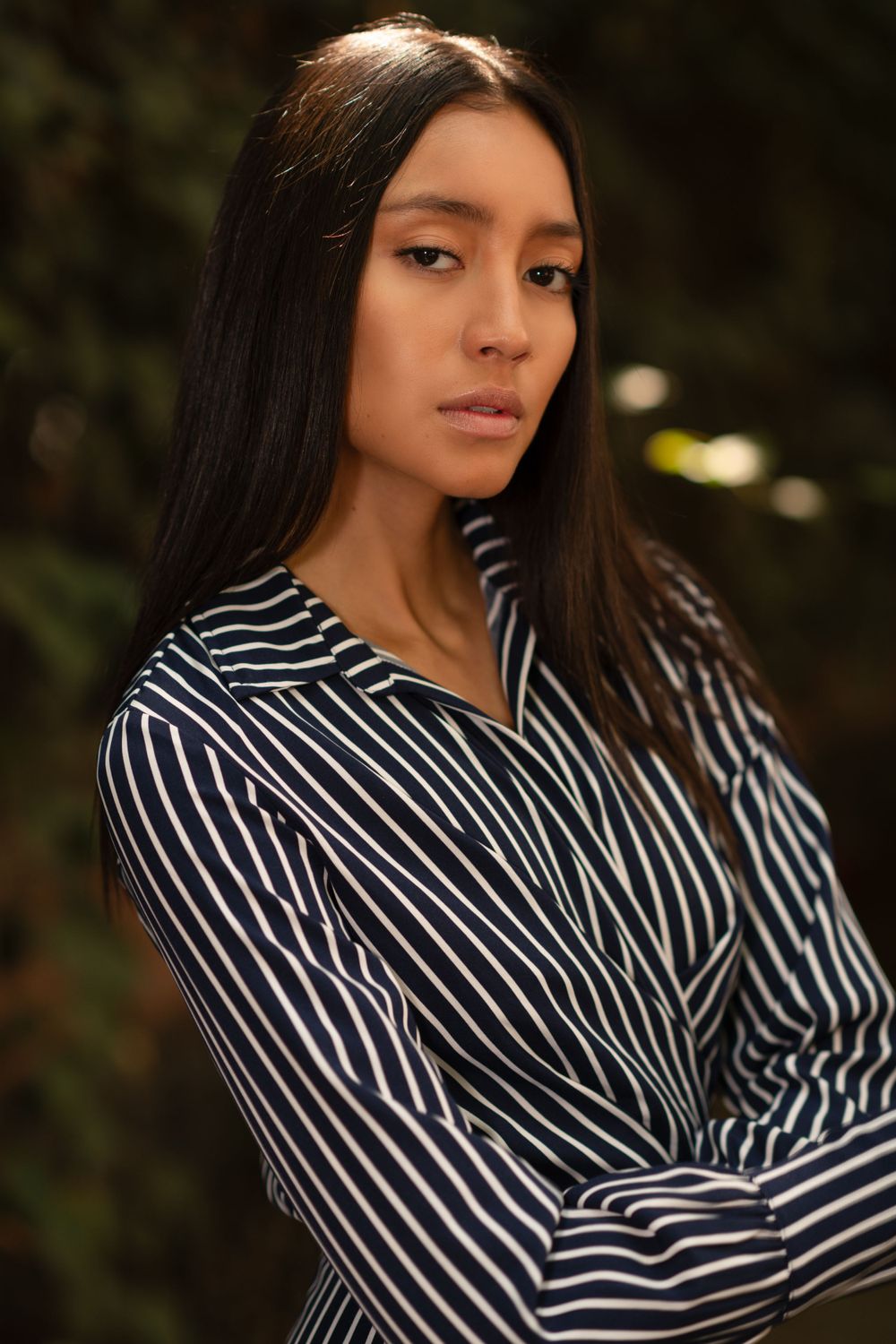 Fashion portrait of a young woman with long dark hair wearing a black and white striped shirt in an outdoor setting.