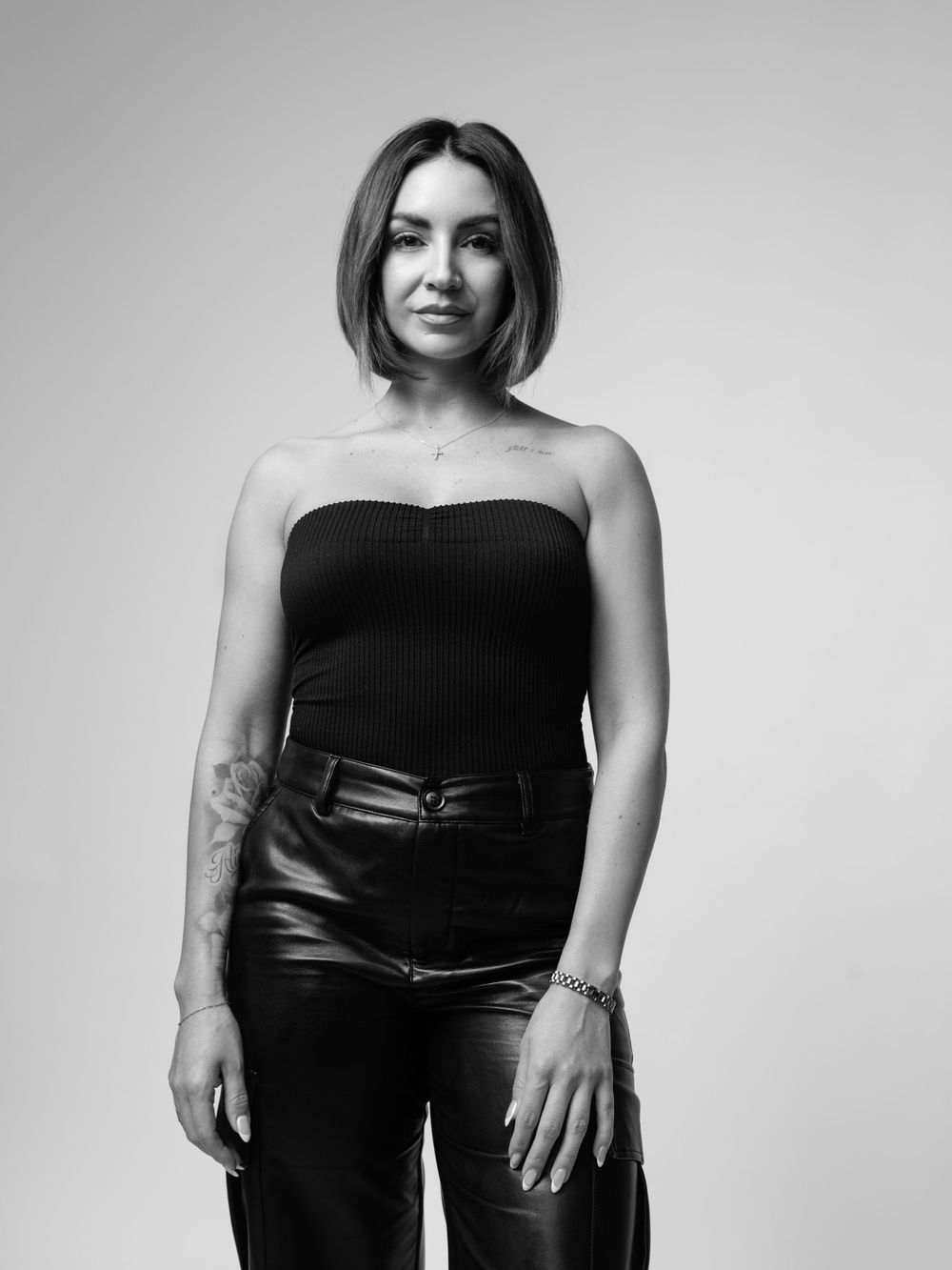 Black and white studio portrait of someone in a strapless top and leather pants posing against a plain backdrop.