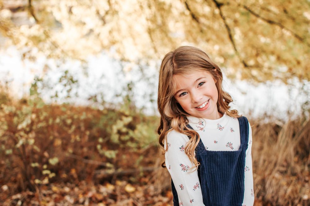 Young child in blue overalls smiling during fall outdoor portrait session in Tri Cities, Washington.