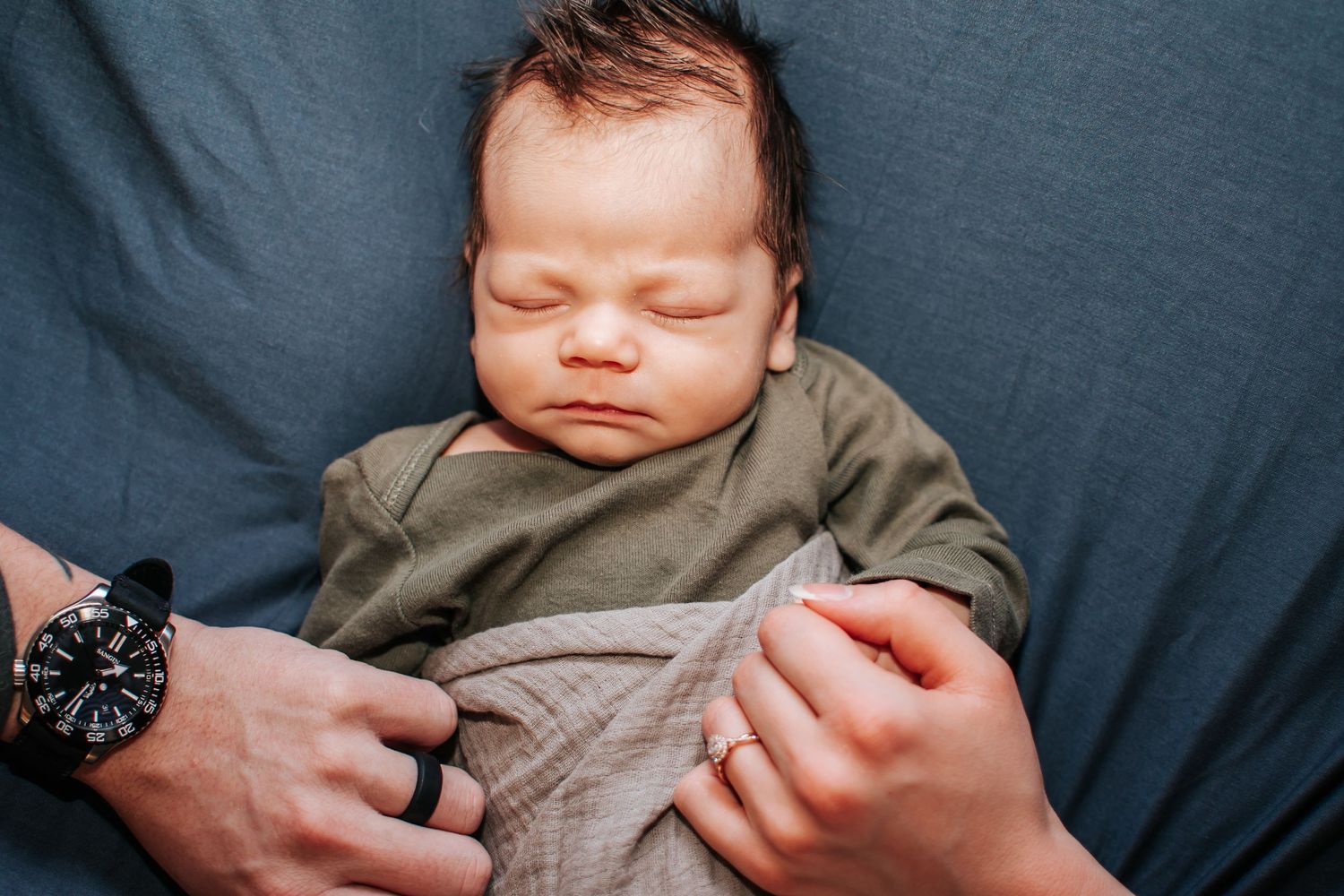 Sleeping newborn baby in grey onesie being held by parent's hands in Tri Cities, Washington photo studio.