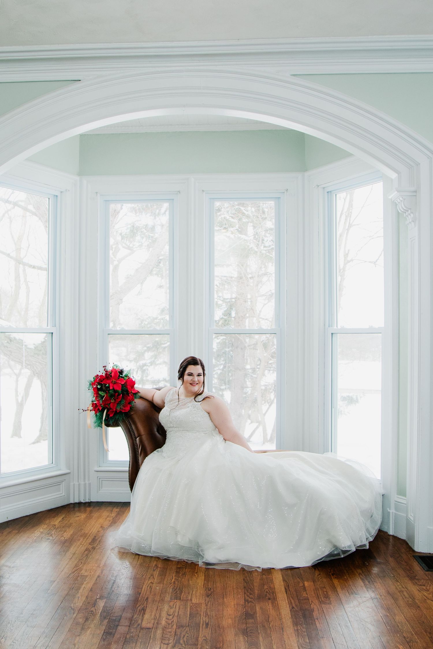Wedding at Gallagher Barn in Medina, N.Y. Bride poses with Christmas bouquet in bay window setting at the Gallagher Barn in Medina, N.Y.