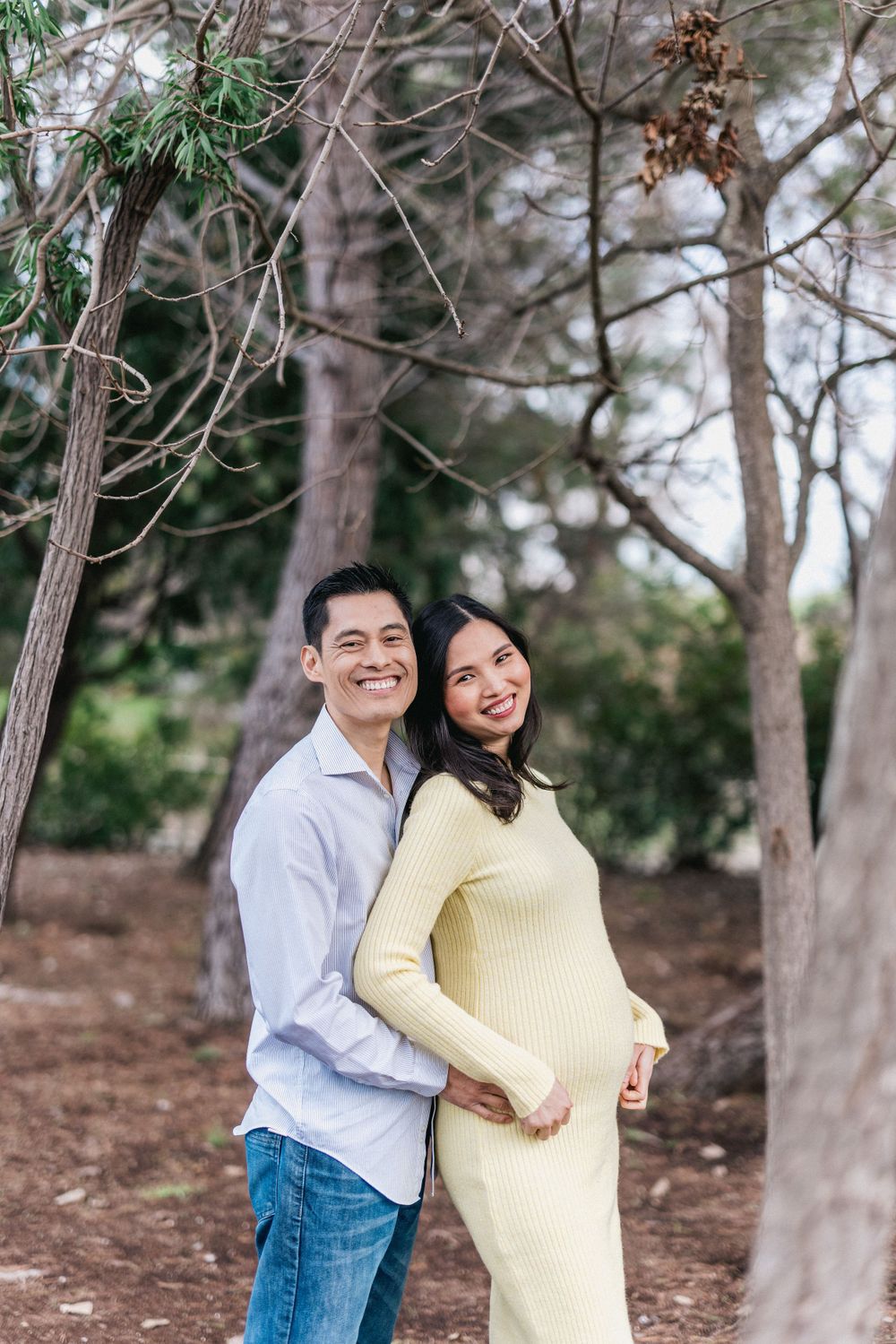 Couple embracing outdoors among tall trees in a natural setting.