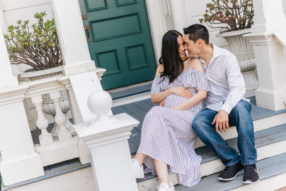 Couple sits on white stone steps near green door during maternity photoshoot.