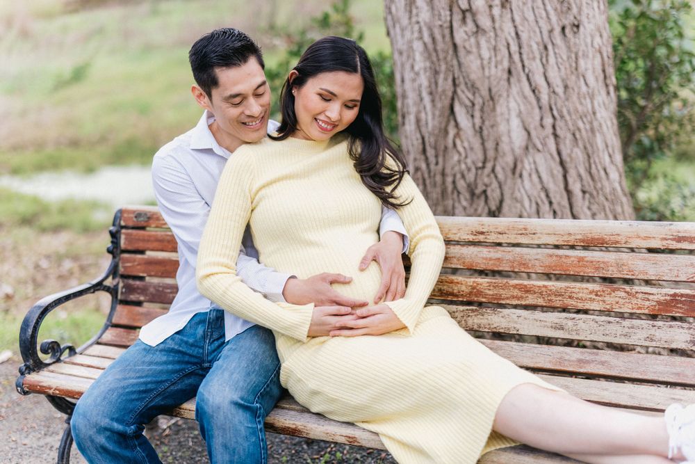 Couple sitting together on wooden park bench surrounded by trees.