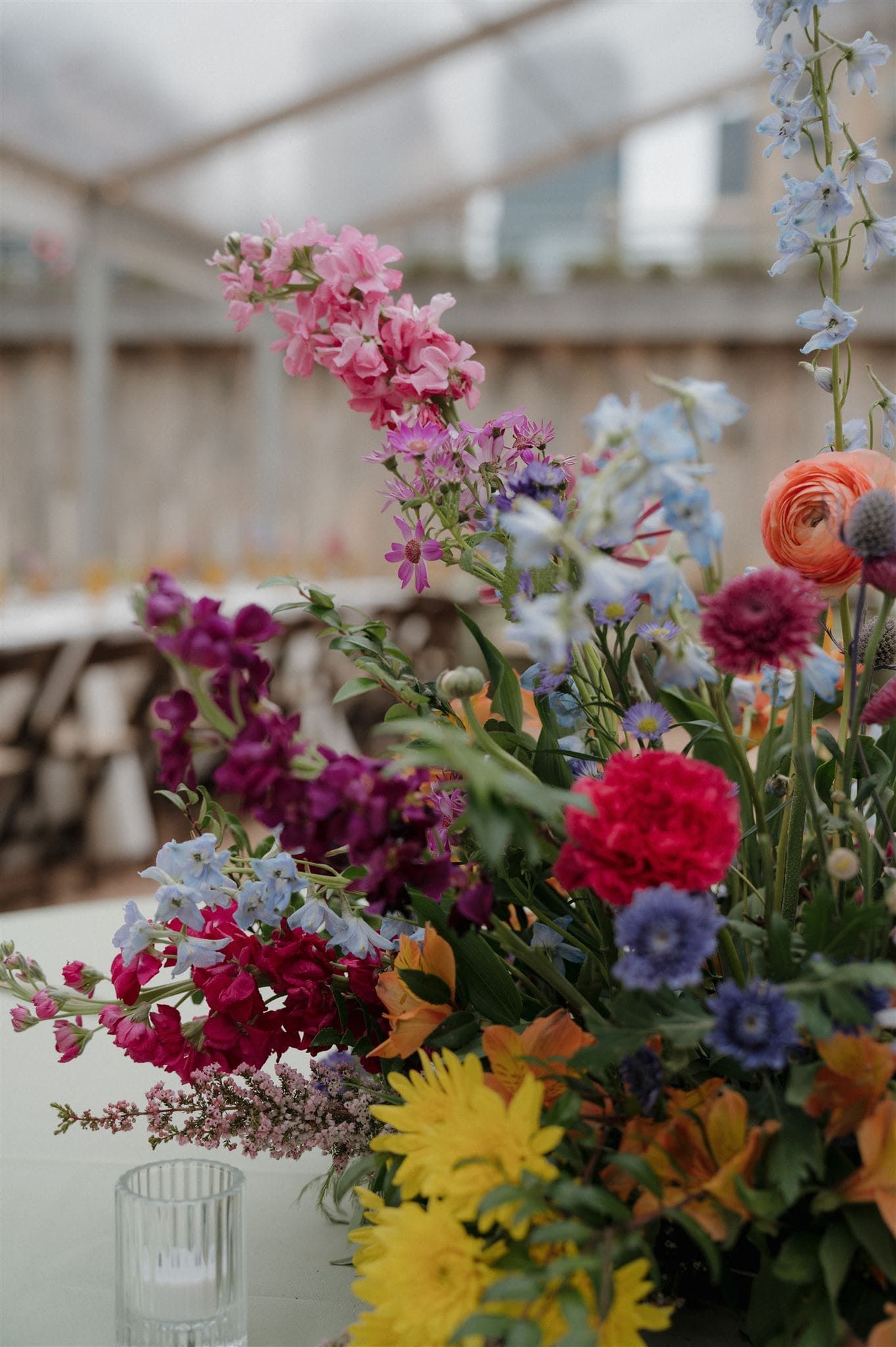 A vibrant floral arrangement with pink snapdragons, yellow daisies, blue delphiniums, and red carnations in a glass vase.